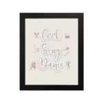 Cook Sing Dance kitchen wall art with pastel pink tones, a beige background, and musical notes. displayed on the wall in a black frame in a white background