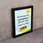 Be Strong And Courageous Psalm 31:24 Bible Verse Wall Art with sun and stars on a sky blue background for kids. displayed on the wall in a black frame