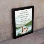 The lakeside scene with a deer and mountains features the verse I Am A Son Of The Most High King in calming colors. displayed on the wall in a black frame