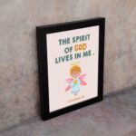 Infidu wall art featuring a cute angel with pink wings and a light blue dress, with the text The Spirit of God lives in me above. displayed on the wall in a black frame