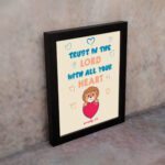 Cute teddy bear holding a heart with Trust in the Lord with all your heart text above, Proverbs 3:5 wall art design. displayed on the wall in a black frame