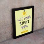 Infidu wall art featuring a lightbulb and the verse Let Your Light Shine from Matthew 5:16 in colorful fonts on a yellow background. displayed on the wall in a black frame