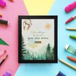 Watercolor wall art featuring a forest scene with the text I Have Called You By Name and You Are Mine from Isaiah 43:1. displayed on the wall in a black frame in a colorful background