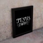 Jesus Christ wall art in white curly font on a black background, showcasing elegant Christian design. displayed on the wall in a white frame