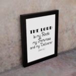 Bible wall art featuring Psalm 18:2 "The Lord Is My Rock, My Fortress, And My Deliverer" in black text on a white background. displayed on the wall in a black frame