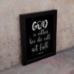 God Is Within Her, She Will Not Fall Psalm 46:5 Bible verse wall art in white text on a black background. displayed on the wall in a black frame