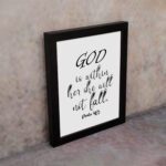 God Is Within Her, She Will Not Fall Psalm 46:5 Christian wall art with black lettering on a white background. displayed on the wall in a black frame