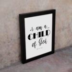 I Am A Child of God John 1:12 Christian Wall Art with black text on a white background displayed on the wall in a black frame