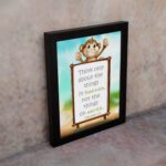 Wall art featuring a happy monkey holding a sign with the verse 'Think only about the things in heaven' from Colossians 3:2. displayed on the wall in a black frame