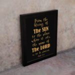 Infidu wall art featuring the text From The Rising of The Sun to The Place Where It Sets, The Name of The Lord is to Be Praised in gold on a black background. displayed on the wall in a black frame