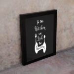 In This Kitchen We Lick The Spoon wall art with white cursive and bold fonts, black background, and stylish cutlery illustrations. displayed on the wall in a black frame