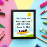 Be Strong And Courageous Psalm 31:24 Bible Verse Wall Art with sun and stars on a sky blue background for kids. displayed on the wall in a black frame in a colorful background