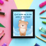 God Holds Me In The Palm Of His Hand Isaiah 49:16 Bible verse wall art for kids featuring a cartoon bear and fluffy clouds. hung on the wall in a black frame in colorful background wall