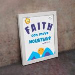 Wall art with the text Faith can move mountains from Matthew 17:20, featuring a sun rising over mountains. displayed on the wall in a white frame