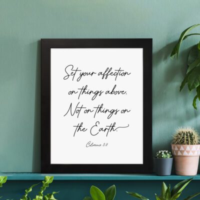 Set Your Affection on Things Above Colossians 3:2 Bible Verse Wall Art on a white background with black text and leaf decorations. displayed on the table in a black frame