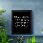 Set Your Affection on Things Above Colossians 3:2 Bible Verse Wall Art on black background with white text and leaf decorations. displayed on the wall in a black frame