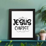 Jesus Christ wall art in black curly font on a white background, showcasing elegant Christian design. displayed on the table in a black frame