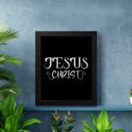 Jesus Christ wall art in white curly font on a black background, showcasing elegant Christian design. displayed on the wall in a white frame