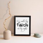 Christian wall art featuring the quote We walk by faith not by sight from Corinthians 5:7 in black text on a white background. displayed on the wall in a black frame