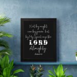 Not By Might Nor By Power Zechariah 4:6 Christian wall art with white text on a black background. displayed on the wall in a black frame