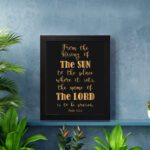 Infidu wall art featuring the text From The Rising of The Sun to The Place Where It Sets, The Name of The Lord is to Be Praised in gold on a black background. displayed on the wall in a black frame