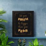 Infidu wall art with the text "Let your faith be bigger than your fear" in gold and bronze, with the Bible verse Hebrews 13:6 on a black background. displayed on the wall in a black frame