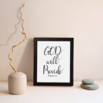 Infidu wall art with the text "GOD will provide" in black font on a white background, featuring the Bible verse Philippians 4:19. displayed on the wall in a black frame