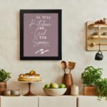 In This Kitchen We Lick The Spoon kitchen wall art with playful spoon illustration on a mauve background. There is a vegetable table, and above it, there is wall art.