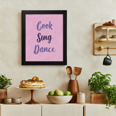 Infidu Cook Sing Dance Kitchen Wall Art with bold navy-blue text on soft pink background, framed in black, modern and lively kitchen design. There is a vegetable table, and above it, there is wall art.