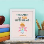 Infidu wall art featuring a cute angel with pink wings and a light blue dress, with the text The Spirit of God lives in me above. displayed on the table in a white frame