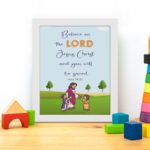 Wall art with a green field, trees, and cartoon figures of Jesus and children, featuring the text 'Believe in the Lord Jesus Christ, and you will be saved. displayed on the table in a white frame