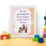 Wall art depicting Jesus as the Good Shepherd with children, featuring the verse I am the good shepherd from John 10:11. displayed on the table in a white frame