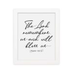 The Lord Remembers Us And Will Bless Us - Psalm 115:12 Bible Verse Wall Art on a white background with black text. hung on the wall in a white frame