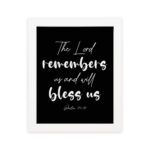 The Lord Remembers Us And Will Bless Us - Psalm 115:12 Bible Verse Wall Art on a black background with white text. hung on the wall in a white frame