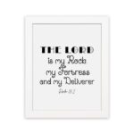 Bible wall art featuring Psalm 18:2 "The Lord Is My Rock, My Fortress, And My Deliverer" in black text on a white background. hung on the wall in a white frame