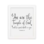 You Are The Temple Of God" Bible Wall Art with gold text on a black background from 1 Corinthians 3:16. hung on the wall in a white frame