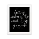 Christian wall art with the quote 'Getting wisdom is the wisest thing you can do' from Proverbs 4:7 in white text on a black background. hung on the wall in a white frame