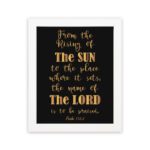 Infidu wall art featuring the text From The Rising of The Sun to The Place Where It Sets, The Name of The Lord is to Be Praised in gold on a black background. hung on the wall in a white frame