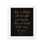 Proverbs 31:25 Christian Wall Art - She Is Clothed With Strength And Dignity, Gold Text on Black Background, hung on the wall in a white frame