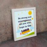 Be Strong And Courageous Psalm 31:24 Bible Verse Wall Art with sun and stars on a sky blue background for kids. displayed on the wall in a white frame