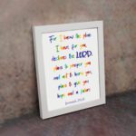 Colorful wall art featuring Jeremiah 29:11, For I Know The Plans I Have For You, with rainbow text on a white background. displayed on the wall in a white frame