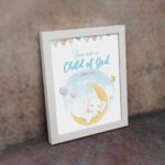 You Are a Child of God wall art featuring a white elephant on a crescent moon with stars and pastel flags. displayed on the wall in a white frame