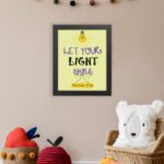 Infidu wall art featuring a lightbulb and the verse Let Your Light Shine from Matthew 5:16 in colorful fonts on a yellow background. displayed on the wall in a black frame