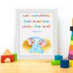 Colorful elephant wall art with the verse "Let everything that breathes praise the Lord!" for kids' room decor. displayed on the table in a white frame