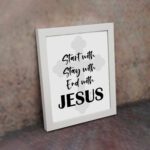 Start With Jesus, Stay With Jesus, End With Jesus Bible Verse Wall Art in Black and White with Light Grey Cross Background displayed on the wall in a white frame