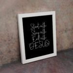 Christian wall art with the phrases Start With Jesus, Stay With Jesus, and End With Jesus in white text on a black background. displayed on the wall in a white frame