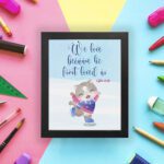 Wall art featuring a joyful bear in winter clothes holding a heart, with the verse We love because He first loved us from 1 John 4:19. displayed on the wall in a black frame with a colorful background