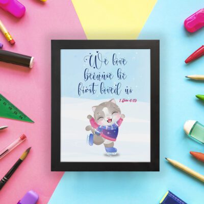 Wall art featuring a joyful bear in winter clothes holding a heart, with the verse We love because He first loved us from 1 John 4:19. displayed on the wall in a black frame with a colorful background