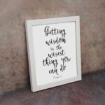 Wall art featuring the quote 'Getting wisdom is the wisest thing you can do' from Proverbs 4:7 on a white background. displayed on the wall in a white frame