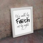 Christian wall art featuring the quote We walk by faith not by sight from Corinthians 5:7 in black text on a white background. displayed on the wall in a white frame